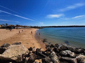 A beach with clear skies, rocky shoreline, and people enjoying the sand.