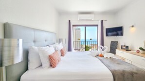 Ein Hotelzimmer mit einem großen Bett, einem Flachbildfernseher, einem Schreibtisch mit Pflanze und einem Balkon mit Blick.