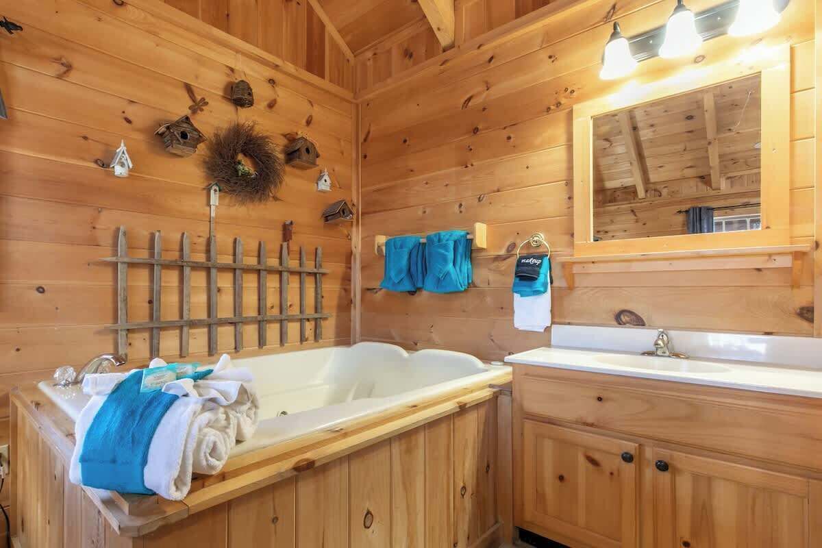 Un baño de cabaña de madera con una bañera, un lavabo y un espejo.