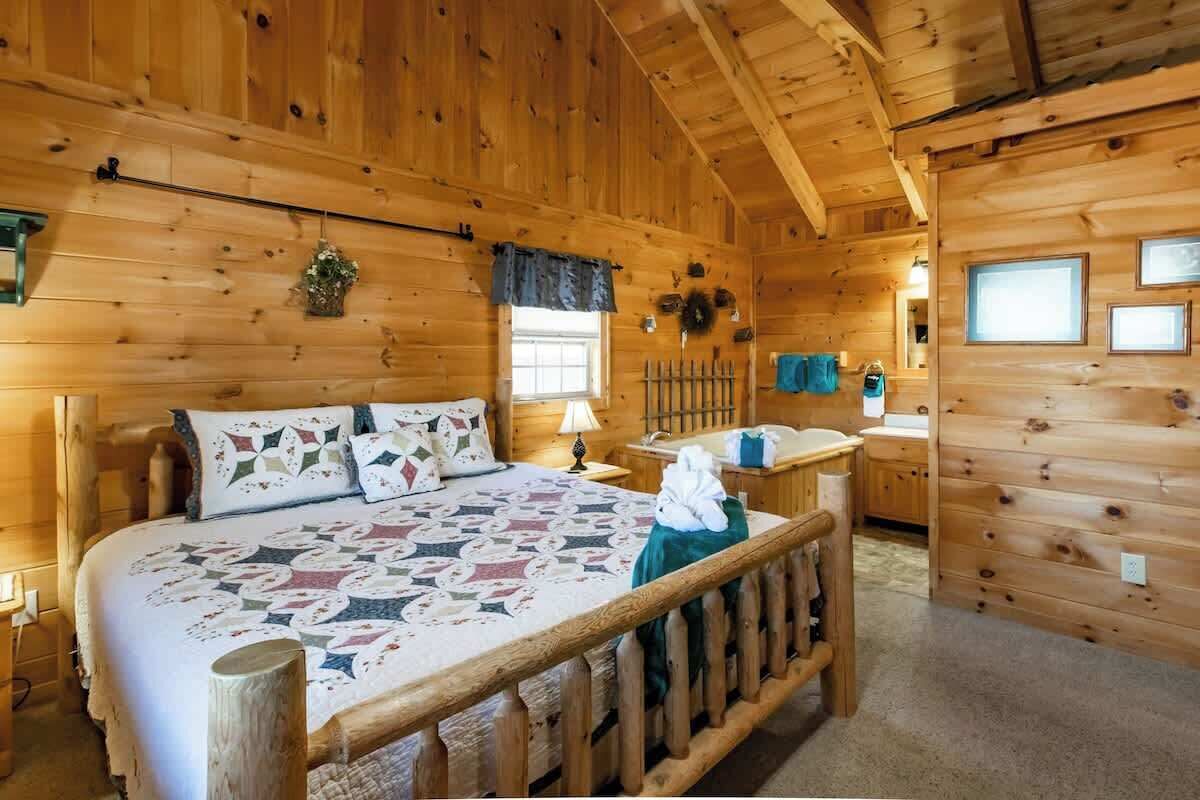 A wooden cabin room with a bed, a nightstand, a window, and a wooden railing.