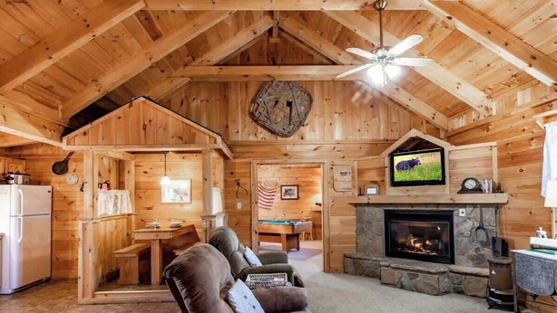 A cozy cabin interior with a fireplace, wooden walls, a ceiling fan, and a television. - Amazing Views! Hot Tub,Pool Table,Fireplace,Relax! (Gatlinburg)