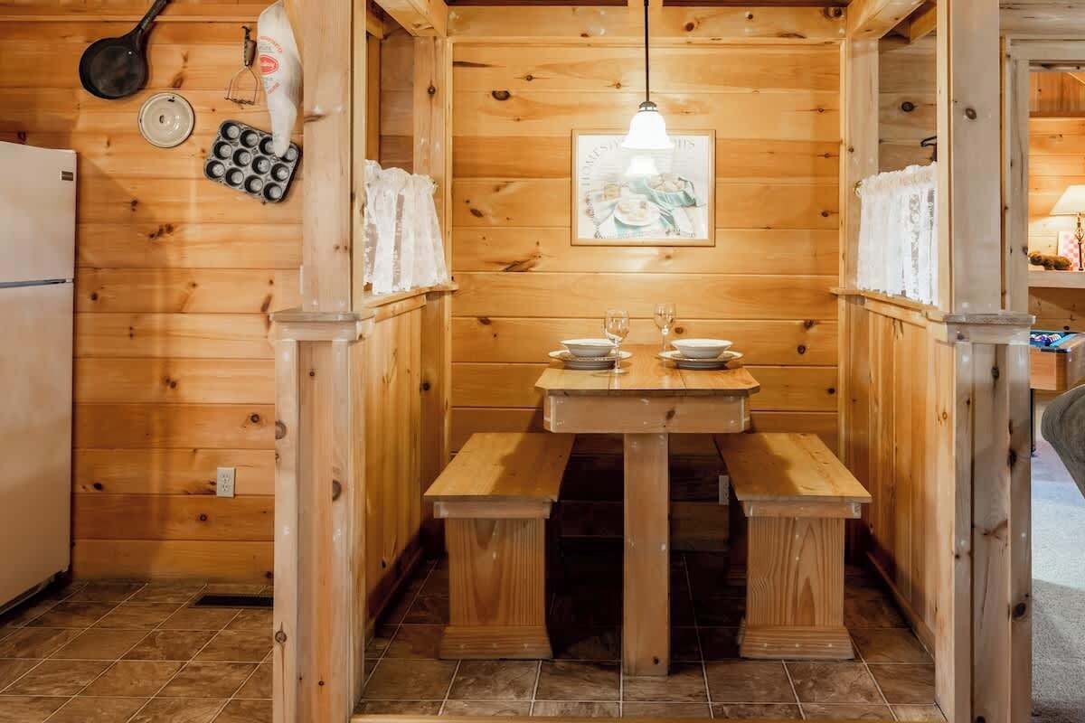 A wooden interior with a wooden table and benches, a hanging light fixture, and a wall-mounted clock.