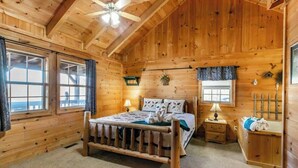 A wooden cabin bedroom with a bed, two bedside tables, a nightstand, a window, and a ceiling fan. - Amazing Views! Hot Tub,Pool Table,Fireplace,Relax! (Gatlinburg)
