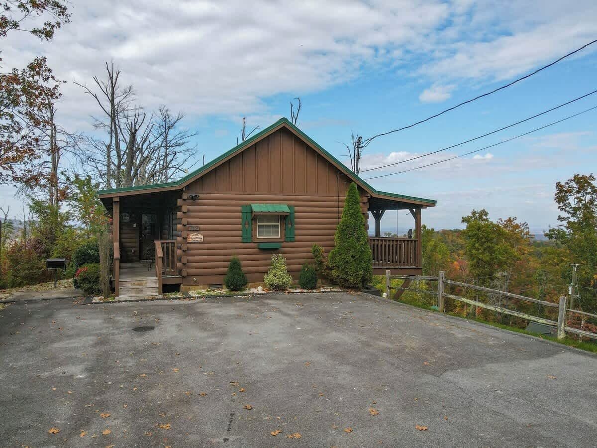 Une cabane rustique en rondins de bois, dotée d’un porche, d’une petite terrasse et d’une allée bordée d’une clôture.