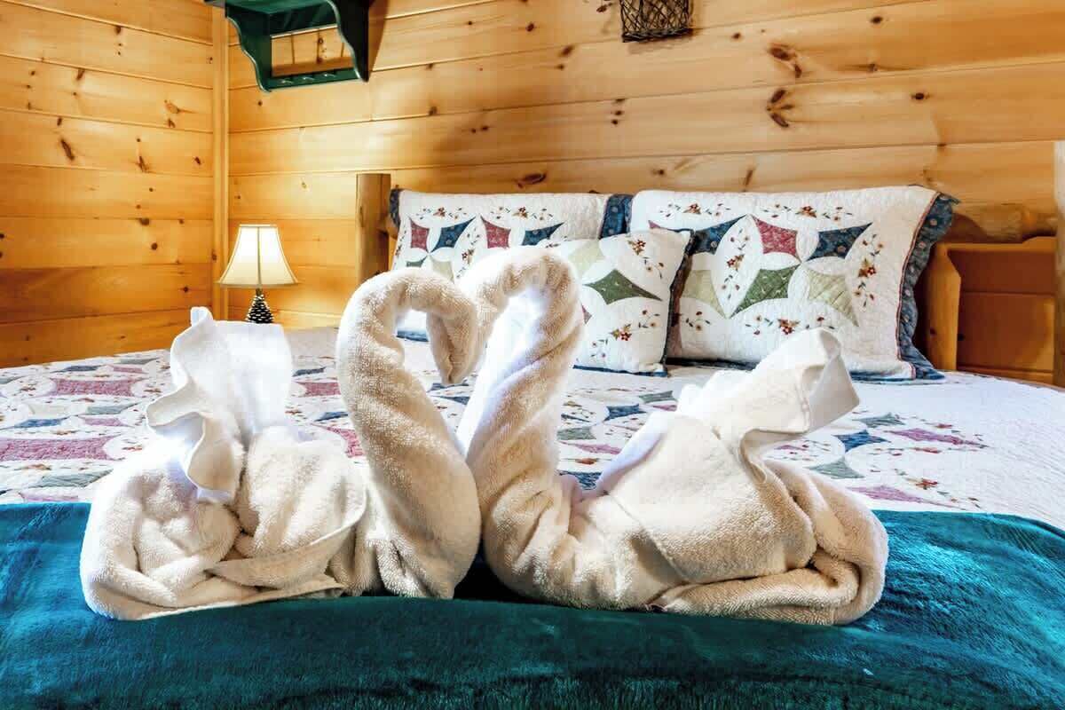 Puisesta mökistä muistuttava huone, jossa on sänky, jossa on kukallinen peitto, sekä kaksi joutsenen muotoista pyyhettä.