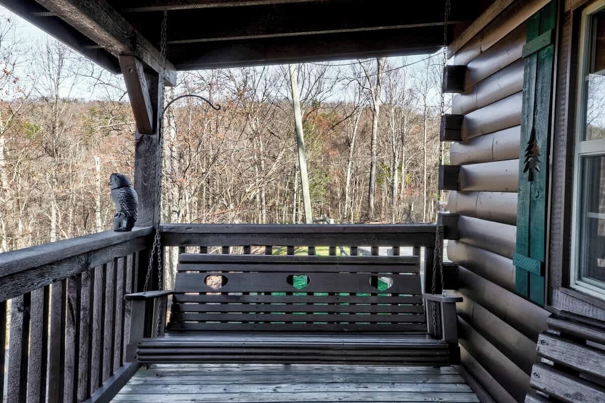 A wooden bench on a porch with a view of a forest.