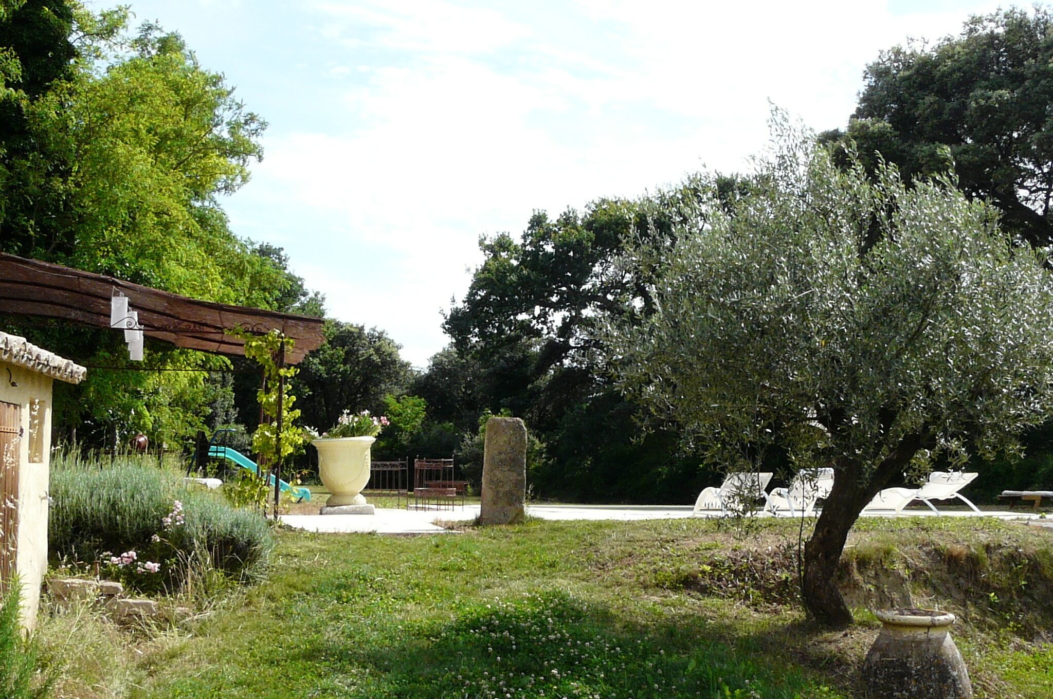 A garden with a pergola, a large planter, and a stone structure.