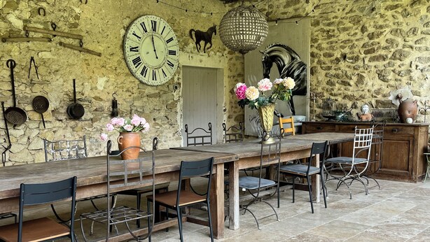 A rustic stone wall with a large clock, a horse sculpture, and a dining area with wooden tables and metal chairs.