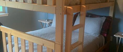 A bunk bed with a wooden frame, a small bedside table, and a wall-mounted shelf.