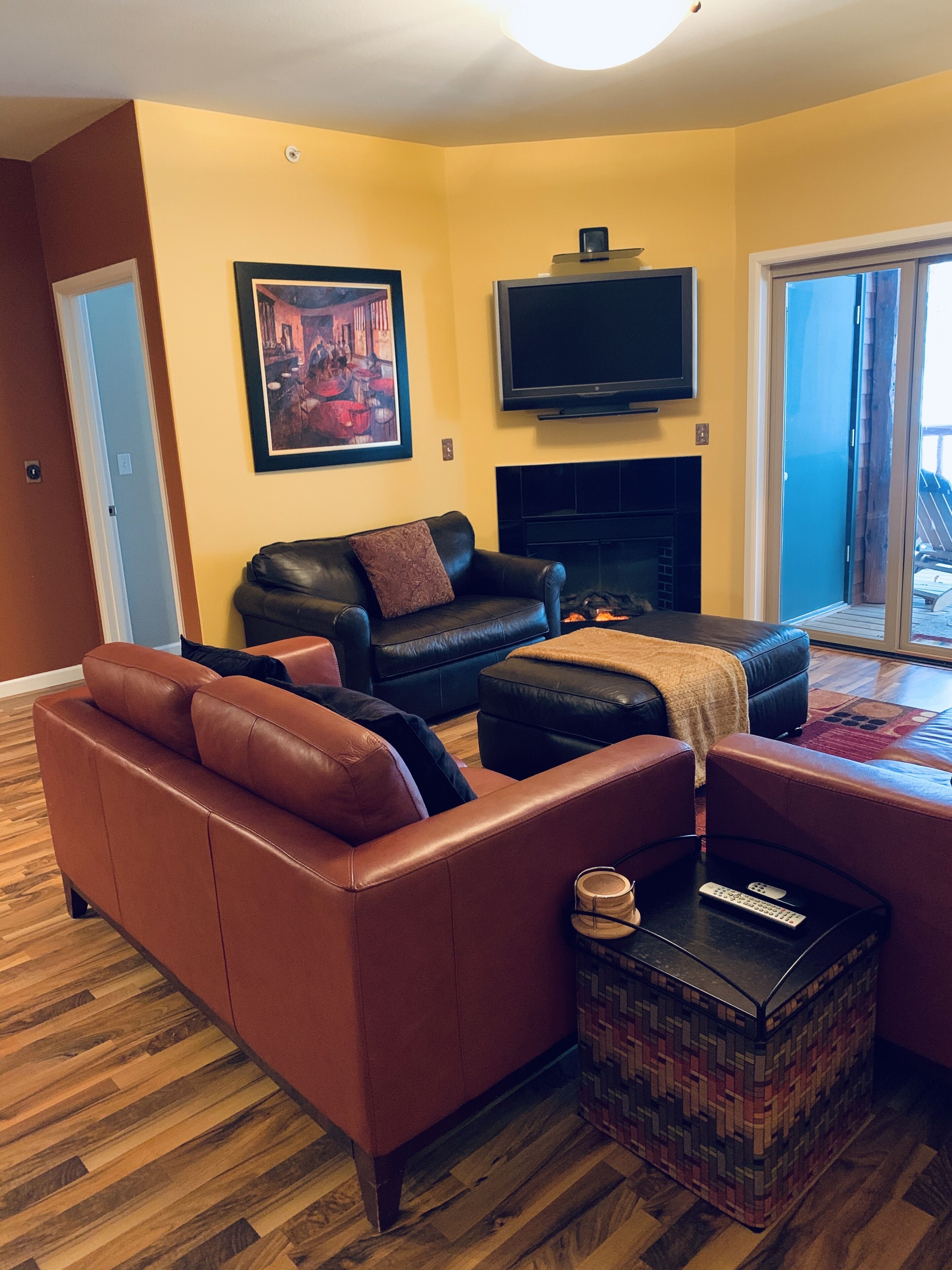 A living room with a fireplace, a TV mounted above it, and a door leading to a balcony.