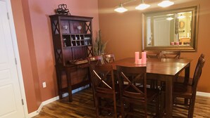 A dining area with a wooden table and chairs, a dark wooden cabinet with wine glasses, and a large mirror on the wall.
