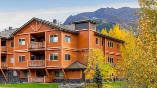 A multi-story lodge with a wooden exterior, balconies, and a view of mountains in the background.