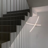 Una escalera moderna con diseño minimalista, que presenta un barandal negro y un elemento de iluminación geométrico en la pared.