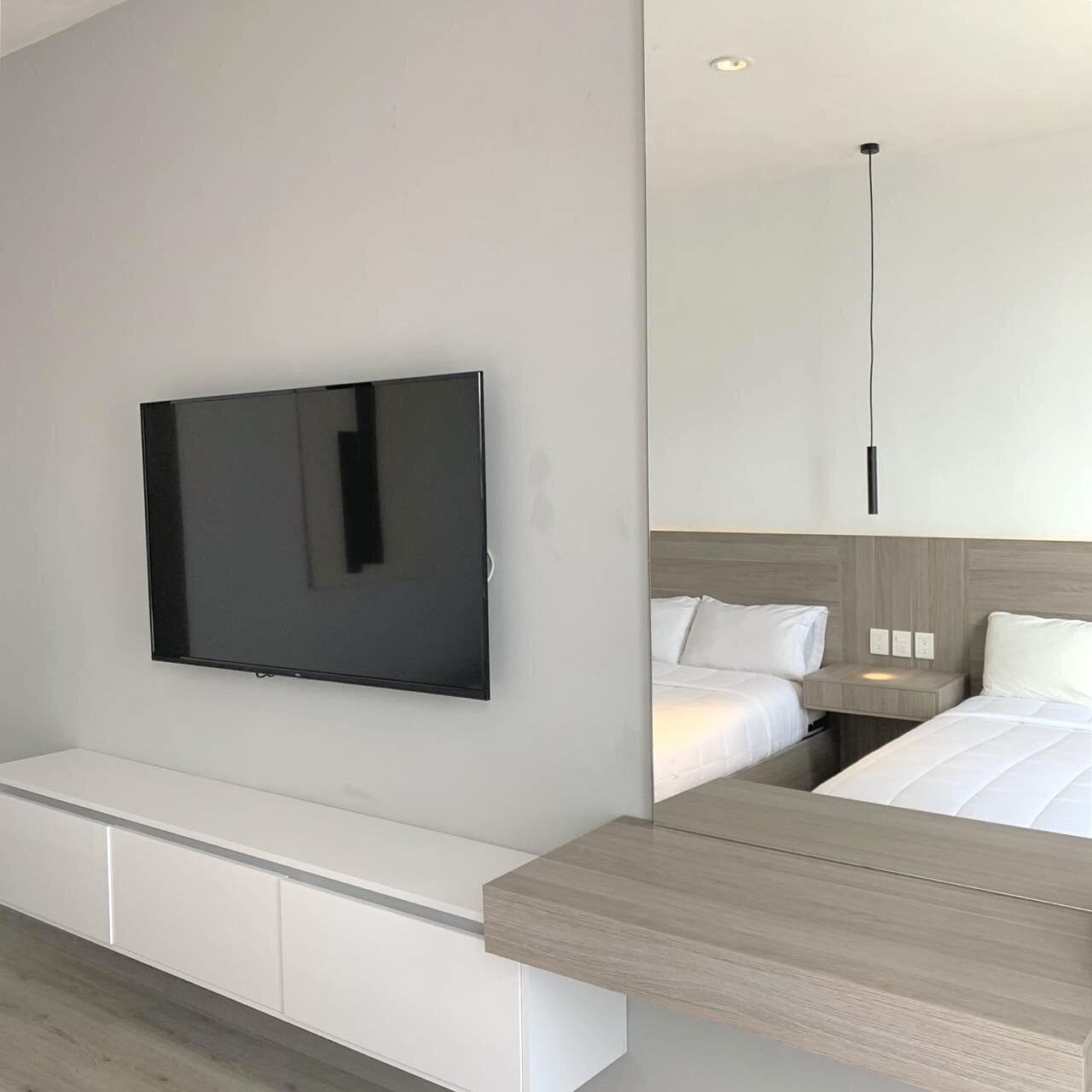A modern hotel room with a flat-screen TV mounted on the wall, a wooden bedside table, and a bed with white bedding.