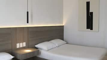 A modern hotel room with two single beds, a bedside table with a lamp, and a wall-mounted artwork.