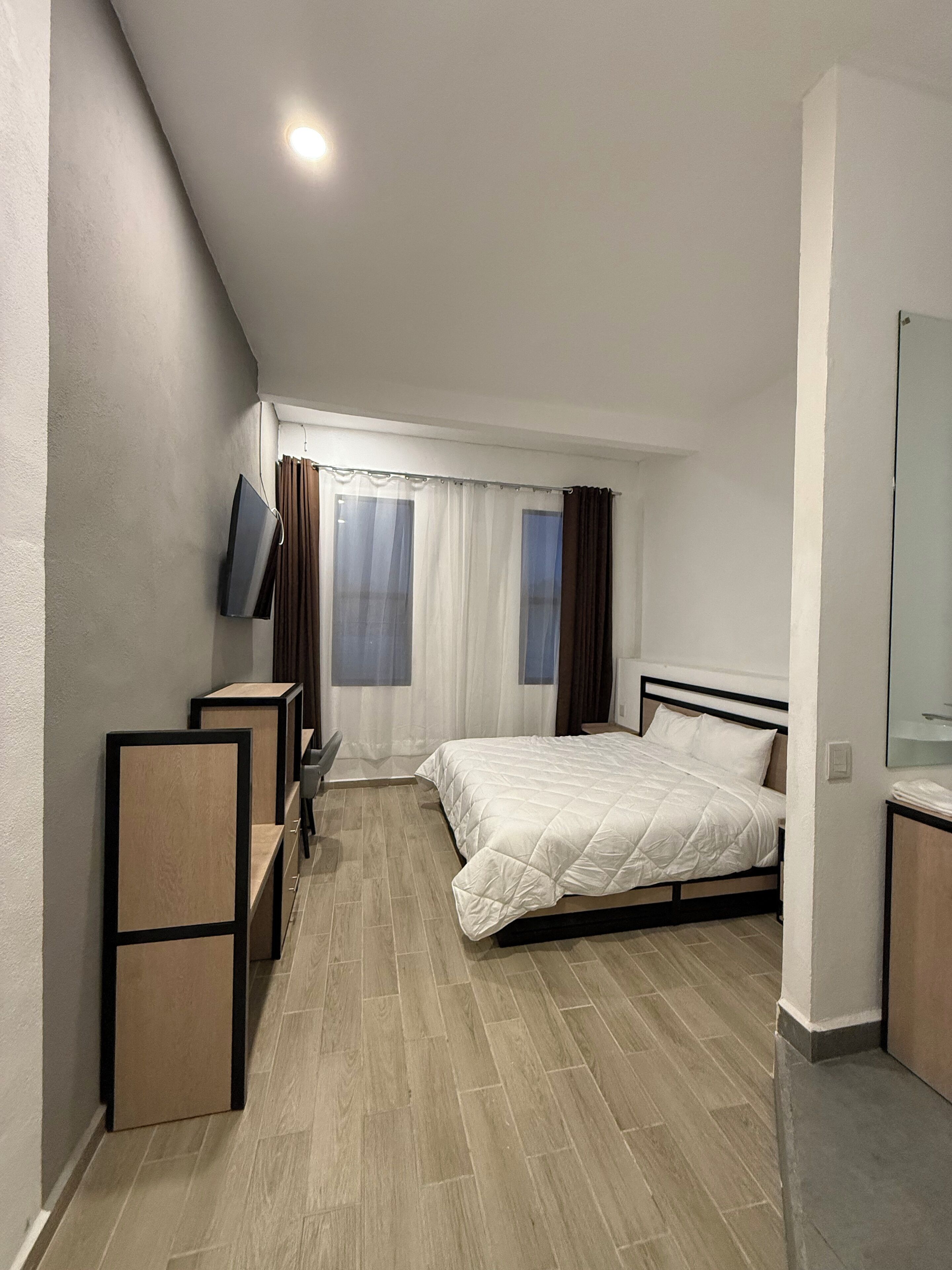 A modern bedroom with a bed, a TV mounted on the wall, and a window with curtains.