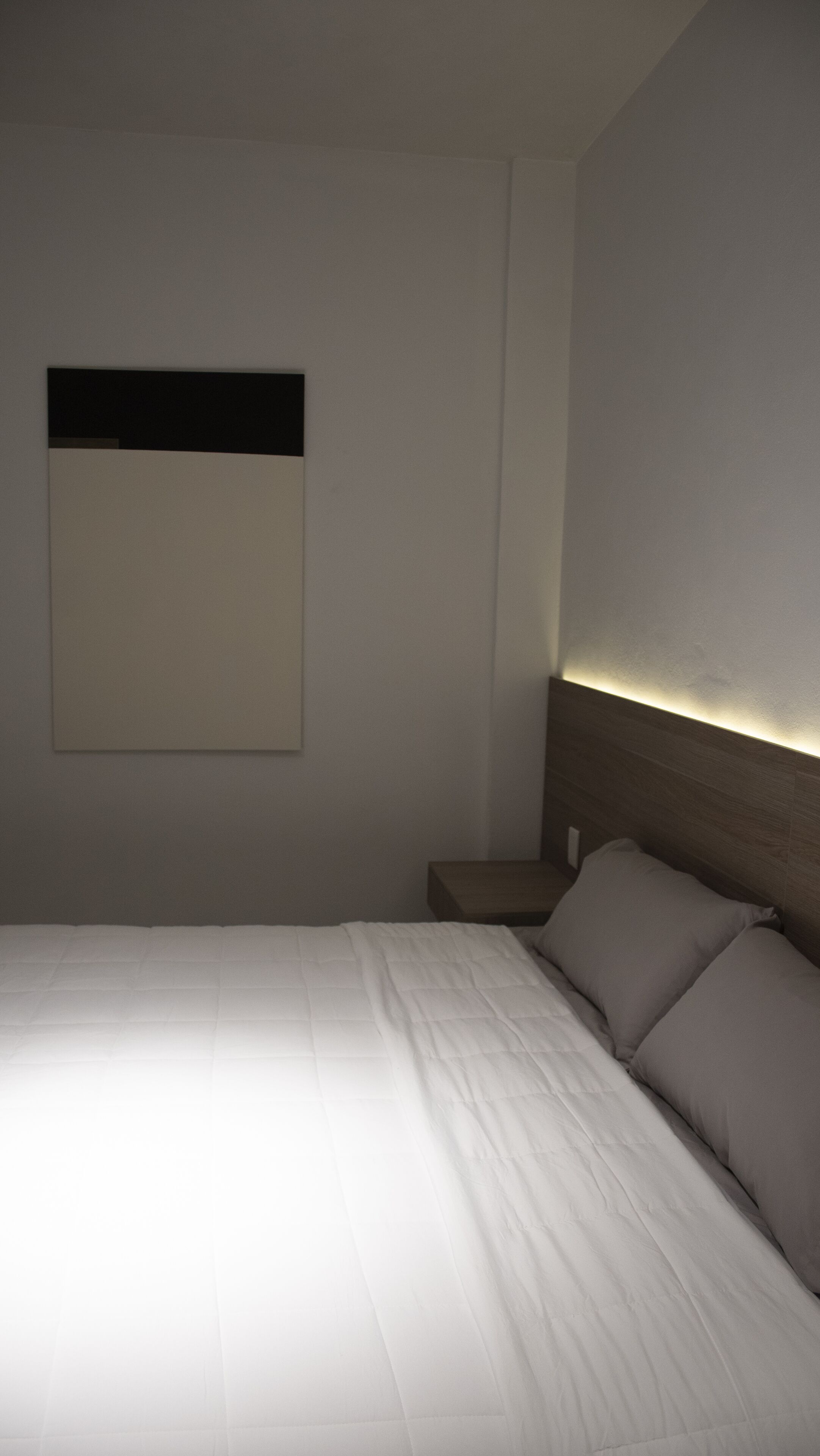Una habitación de hotel con una cama bien hecha, una mesita de noche y una lámpara fijada en la pared.