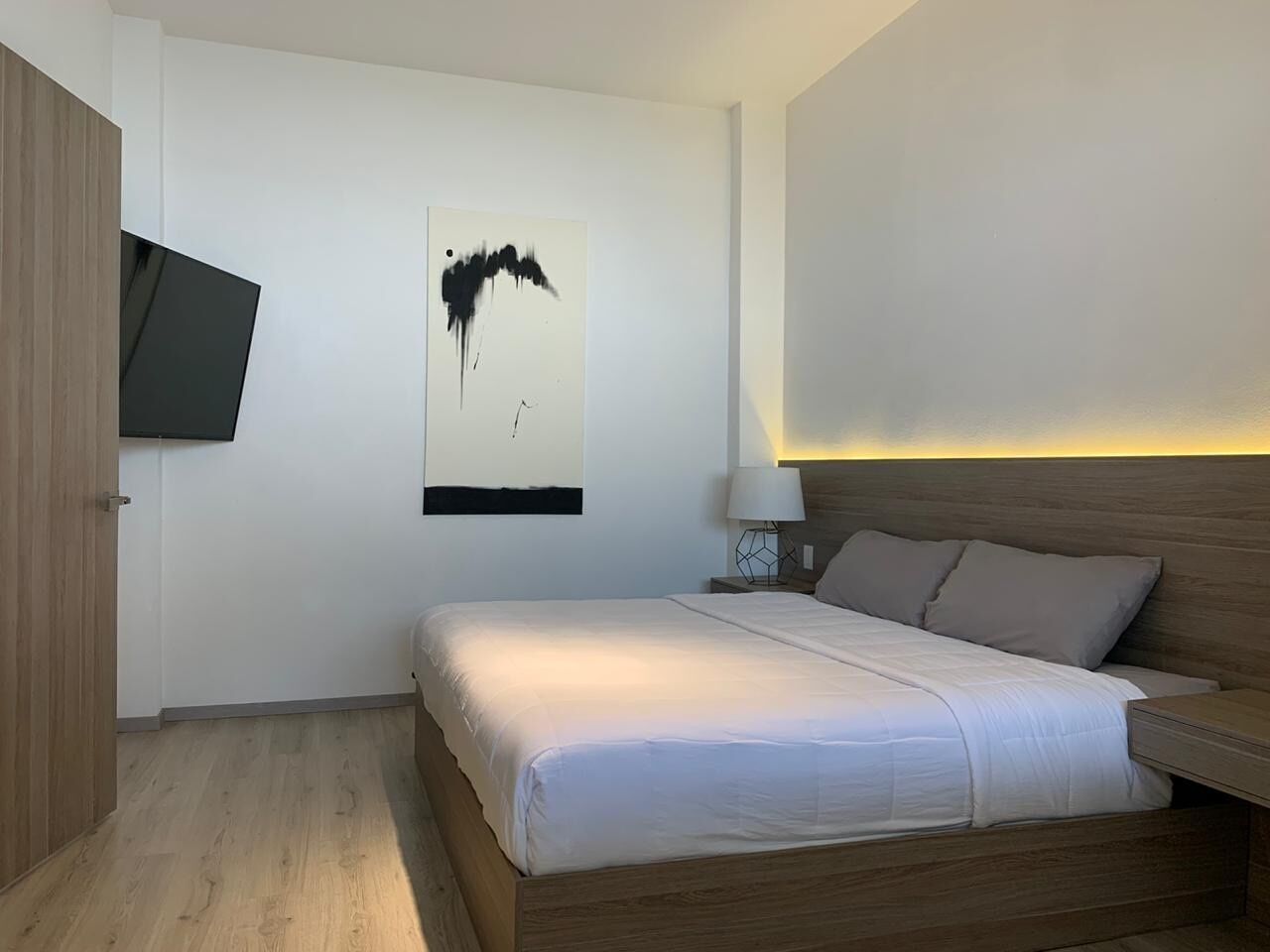 A modern bedroom with a bed, a flat-screen TV mounted on the wall, and a bedside table with a lamp.