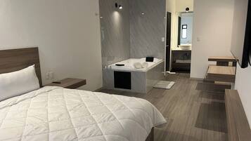 A modern hotel room with a large bed, a bathroom with a bathtub, and a small seating area.