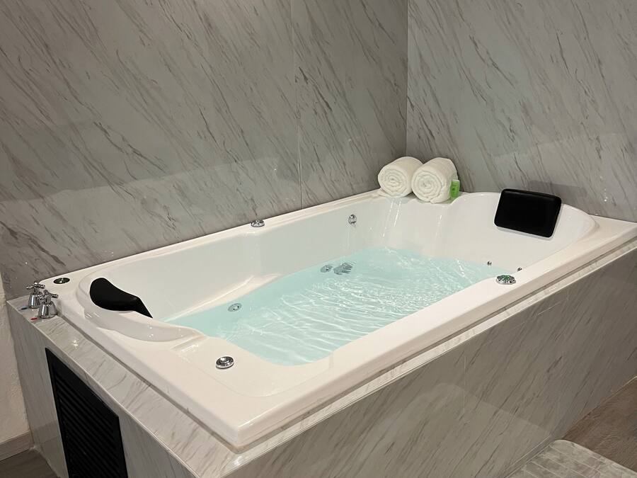 Une salle de bain moderne avec un mur en marbre, une baignoire dotée d’un siège noir et une petite serviette posée sur le bord.