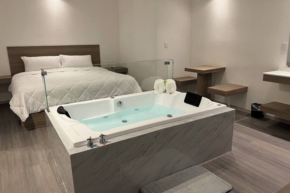 A modern bathroom with a large bathtub, a separate shower area, and a bed with a white quilted bedspread.