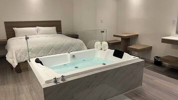 A modern bathroom with a large bathtub, a separate shower area, and a bed with a white quilted bedspread.