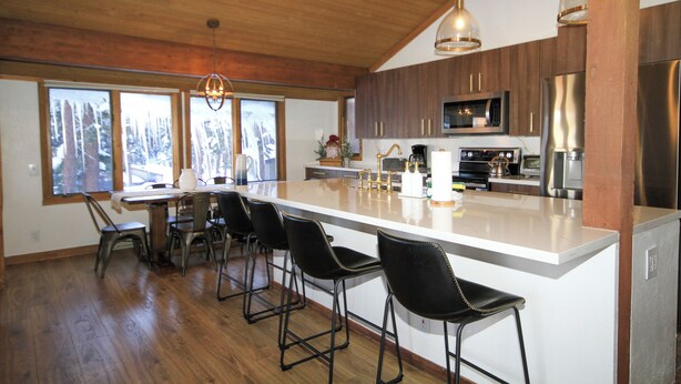 A modern kitchen with a large island, bar stools, and a dining area with a wooden table and chairs. - Mountainback #116, Loft,Corner-no pets accepted (Mammoth Lakes)