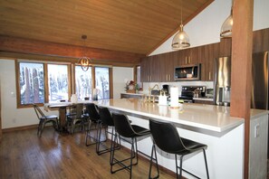 A modern kitchen with a large island, bar stools, and a dining area with a wooden table and chairs. - Mountainback #116, Loft,Corner-no pets accepted (Mammoth Lakes)