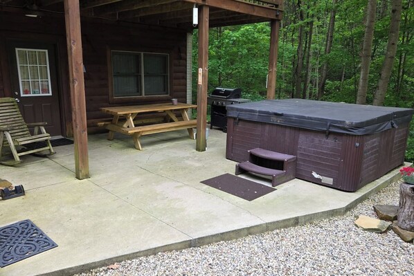 A wooden cabin with a hot tub, picnic table, and steps leading to the hot tub.