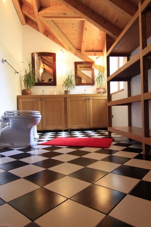 Bathroom features a checkered floor, wooden cabinets, a toilet, and two potted plants, with exposed wooden beams above.