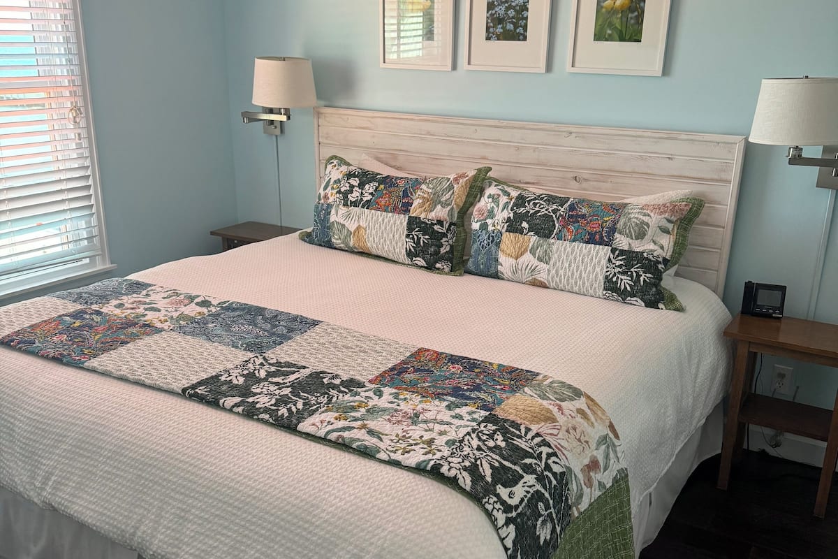 A bedroom with a large bed, two bedside lamps, and three framed pictures on the wall.