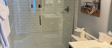 Une salle de bain moderne avec une douche à parois de verre, des toilettes et un lavabo surmonté d’un miroir.