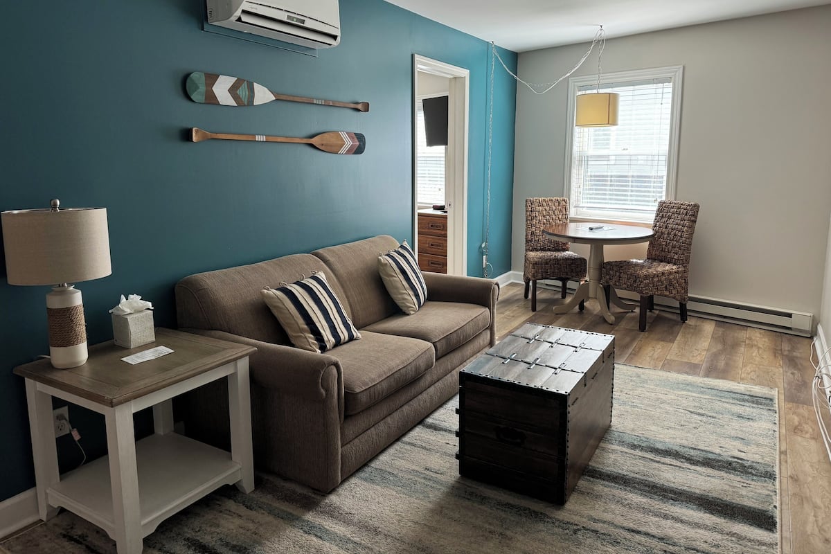 A living room with a brown sofa, striped pillows, a wooden coffee table, a side table with a lamp, and a patterned rug.