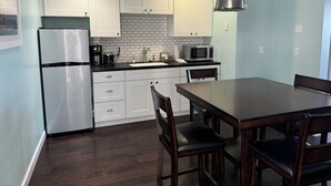Una cocina moderna con armarios blancos, un refrigerador de acero inoxidable, un microondas y una zona de comedor con una mesa y sillas.