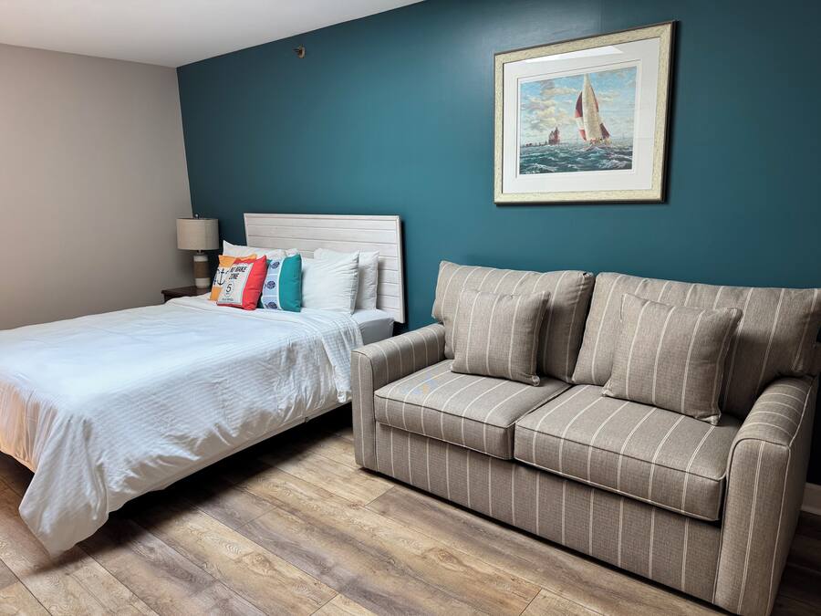 Une chambre à coucher bien rangée, avec un lit, un canapé à rayures, un tableau encadré au mur et une lampe sur la table de chevet.