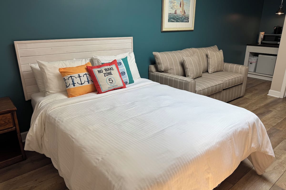 A bedroom with a bed, a sofa, a nightstand, and a painting on the wall.