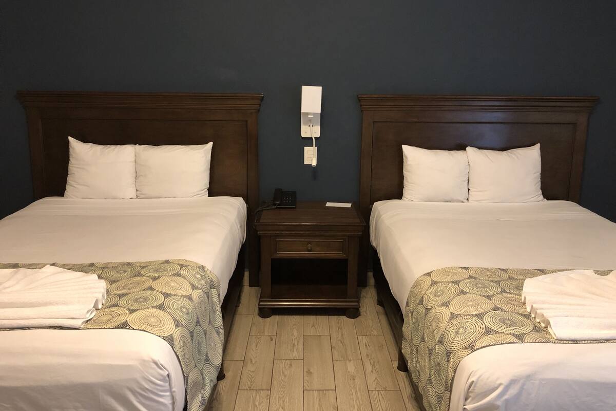 A hotel room with two beds, a nightstand, and a wall-mounted phone.