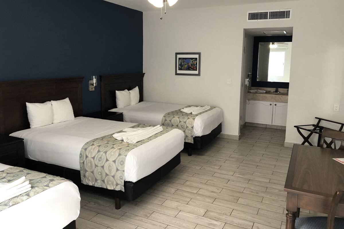 A hotel room with two beds, a ceiling fan, a small bathroom, and a dining area.