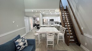 A modern kitchen with white cabinets, a dining area with white chairs, and a staircase with wooden railings.