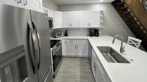 A modern kitchen with white cabinets, stainless steel appliances, and a wooden staircase.