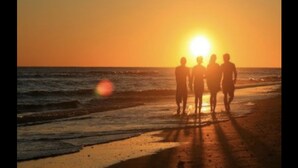 A sunset over the ocean with silhouettes of people standing on the beach.
