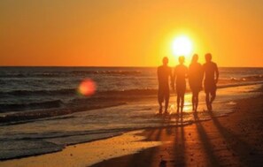A sunset over the ocean with silhouettes of people standing on the beach.