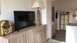 Ein Wohnzimmer mit Flachbildfernseher auf einer Holzkommode, einem Vintage-Radio und einer Lampe.