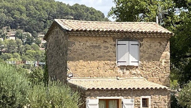 Ein Haus aus Stein mit einem Ziegeldach, einem kleinen Fenster mit Fensterläden und einer Tür.