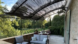 An outdoor patio area with a covered seating area, stone walls, and a view of a garden.