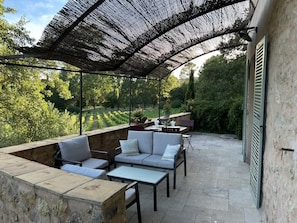 Uma área de pátio ao ar livre com espaço de estar coberto, paredes de pedra e vista para um jardim.