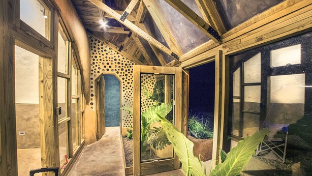 Un intérieur en bois avec une porte en verre donnant sur un espace extérieur, un plafond avec des poutres apparentes et une plante visible.