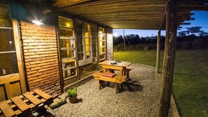 Un espace extérieur aménagé avec une table et des bancs, entouré d’un mur en briques et doté de grandes fenêtres.