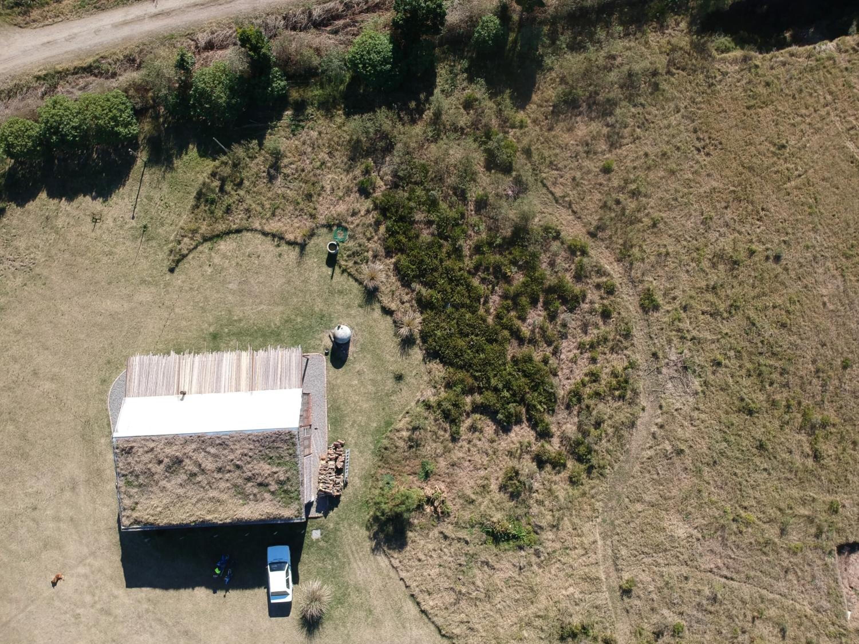 Vue aérienne d’une propriété rurale comprenant un seul bâtiment doté d’un toit plat et d’une zone délimitée par une clôture.