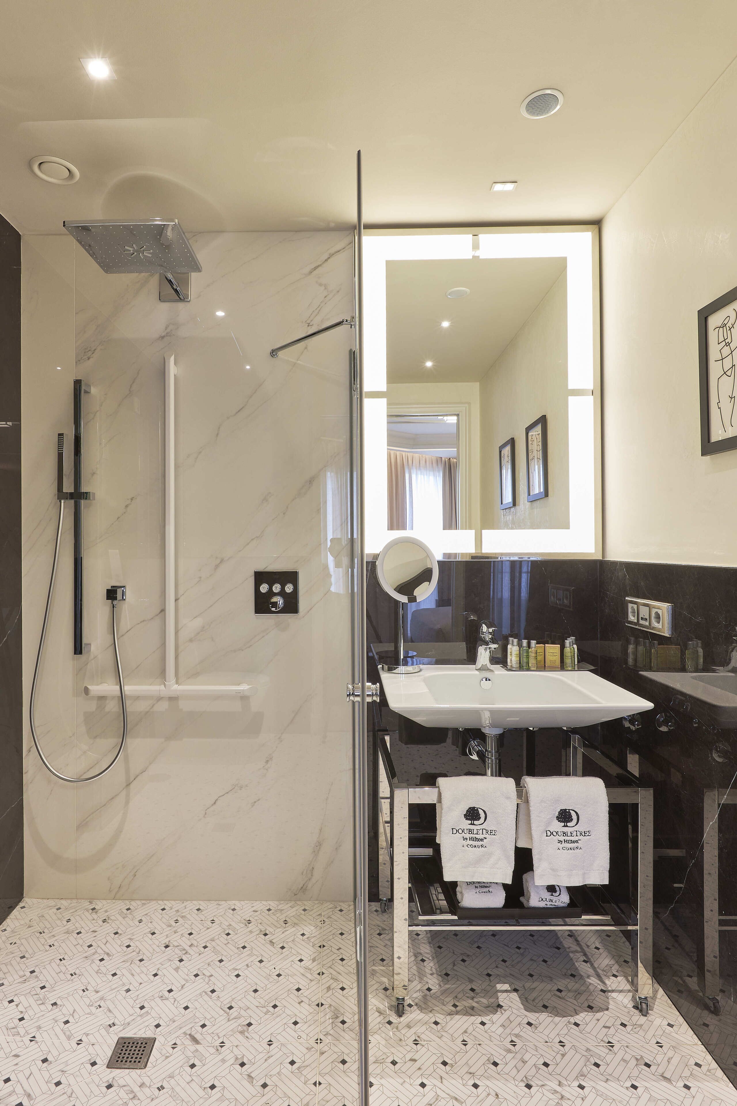 A modern bathroom with a glass-enclosed shower, a large mirror, and a vanity with two towels.